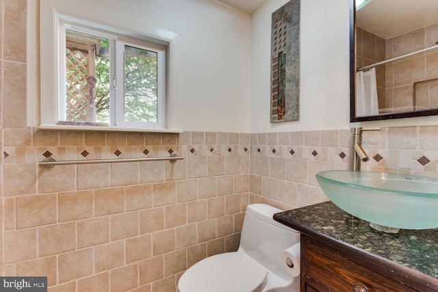 bathroom with a wainscoted wall, toilet, tile walls, a shower with shower curtain, and vanity