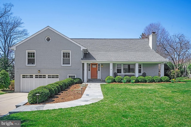 split level home featuring brick siding, a garage, a front yard, a chimney, and driveway