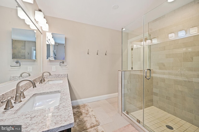 bathroom with baseboards, a sink, a stall shower, and double vanity