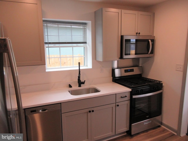 kitchen with light countertops, wood finished floors, gray cabinets, a sink, and appliances with stainless steel finishes