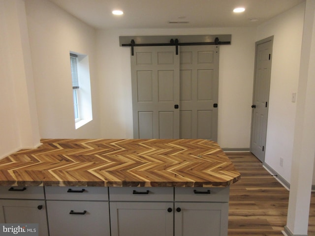unfurnished bedroom with a barn door, dark wood-style floors, and recessed lighting