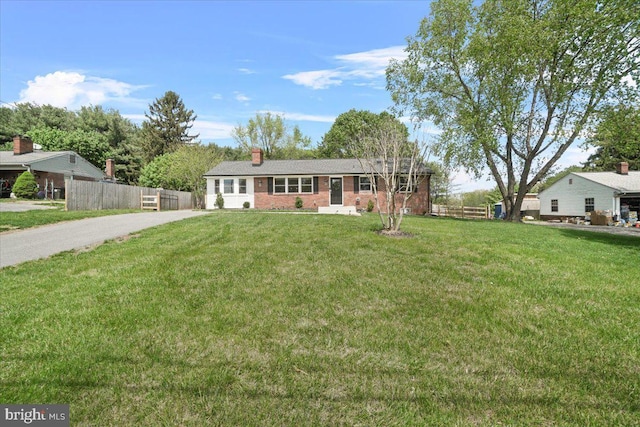 ranch-style house with a chimney, a front yard, brick siding, fence, and aphalt driveway