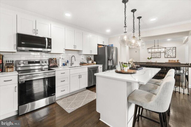 kitchen featuring appliances with stainless steel finishes, a sink, tasteful backsplash, a kitchen island, and dark wood-type flooring
