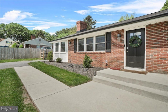 view of front of house with fence, a chimney, and brick siding