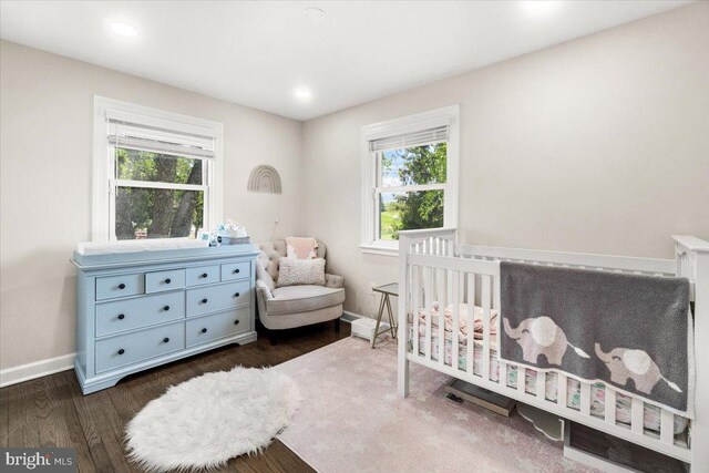 bedroom with baseboards, a crib, dark wood-style floors, and multiple windows