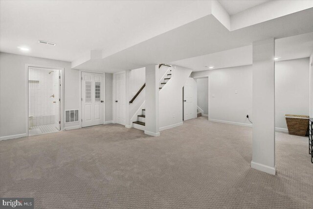 finished below grade area featuring light colored carpet, stairs, baseboards, and visible vents