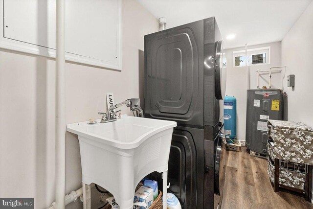 washroom with laundry area, a sink, wood finished floors, stacked washer and clothes dryer, and electric water heater