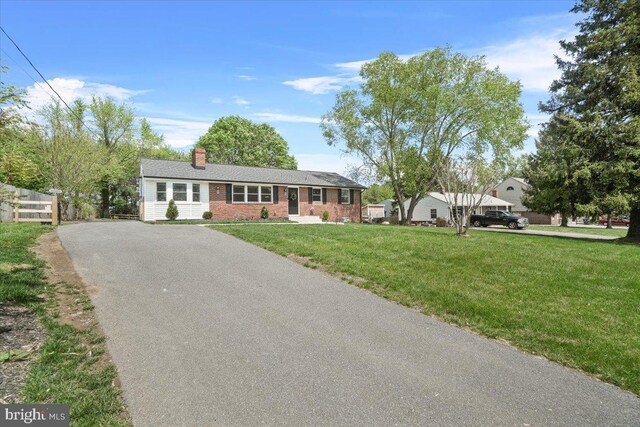 ranch-style house featuring driveway, a chimney, brick siding, fence, and a front lawn