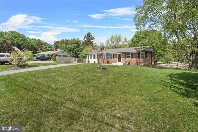 single story home featuring concrete driveway, brick siding, fence, and a front yard