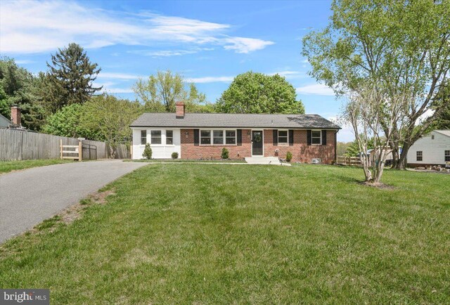ranch-style house with fence, aphalt driveway, brick siding, a front yard, and a chimney