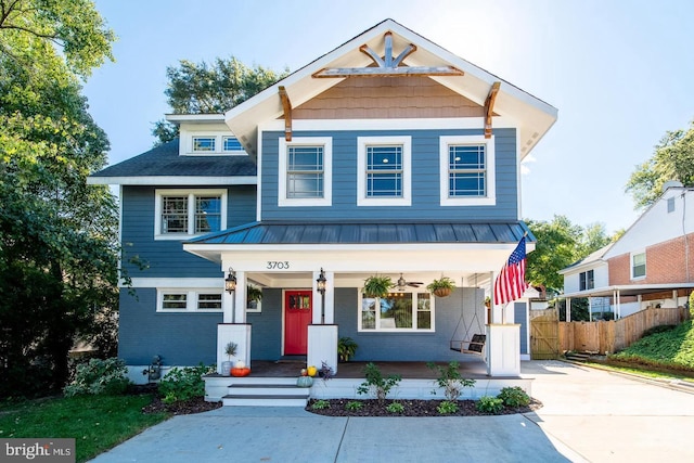 view of front of home with covered porch, brick siding, fence, concrete driveway, and metal roof
