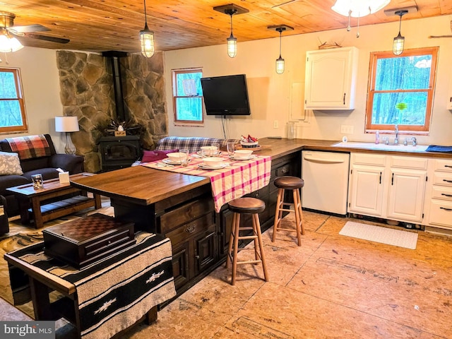 kitchen featuring a wood stove, white cabinetry, wood ceiling, a sink, and dishwasher
