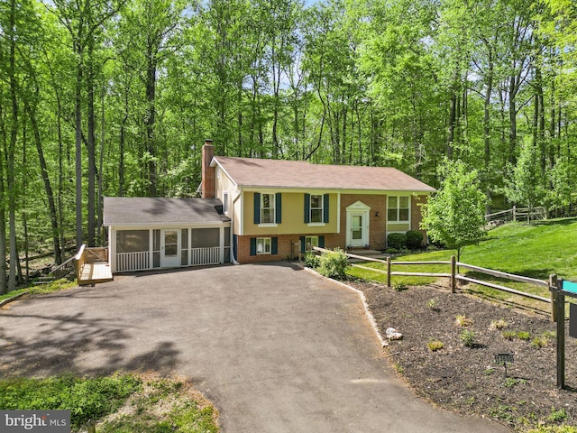 view of front of property with a chimney, aphalt driveway, fence, brick siding, and a sunroom