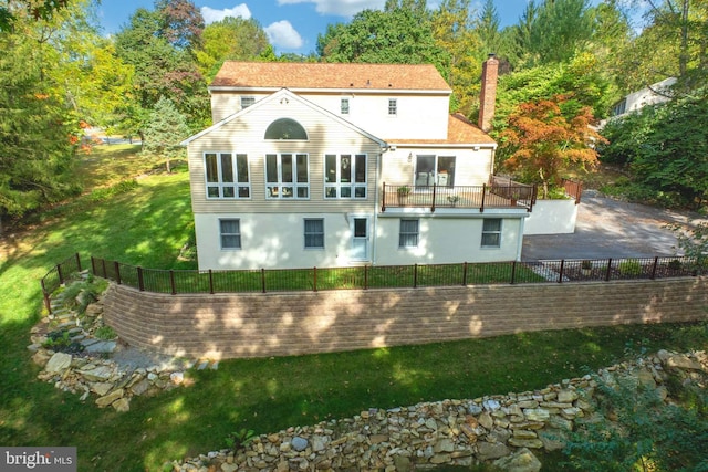 rear view of property featuring a balcony, a yard, a fenced backyard, a chimney, and stucco siding