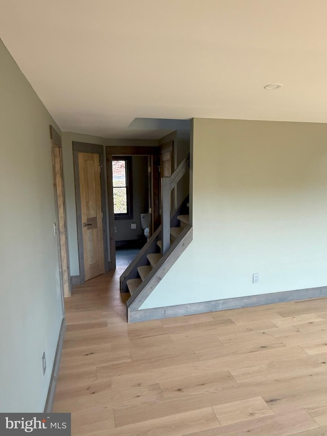hall featuring light wood-style floors, baseboards, and stairs
