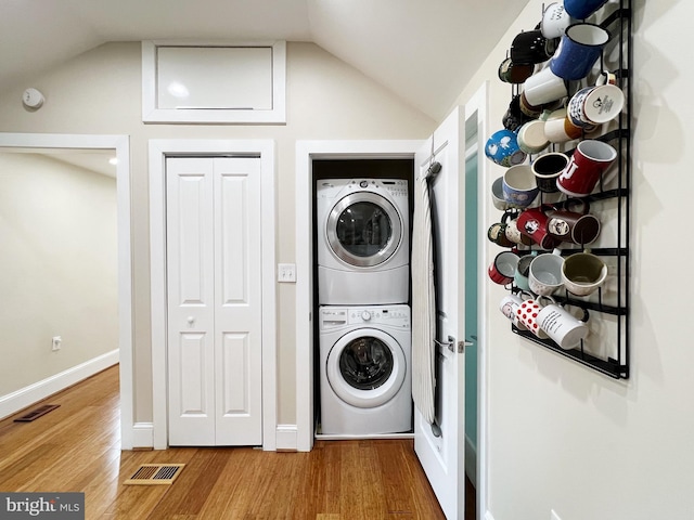 washroom with wood finished floors, stacked washer and dryer, laundry area, baseboards, and visible vents