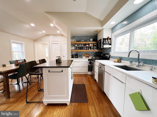 kitchen with vaulted ceiling, a kitchen island, appliances with stainless steel finishes, and a sink