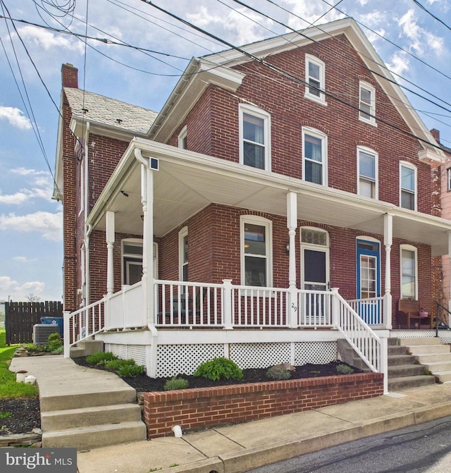 view of front of home featuring brick siding, a chimney, and covered porch