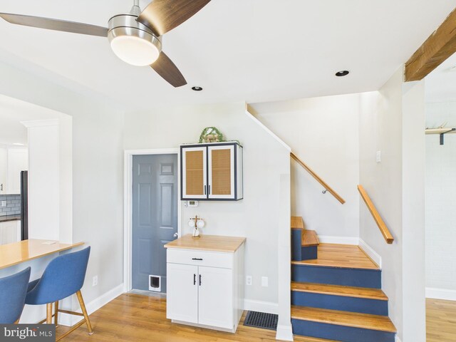 interior space with light wood-type flooring, a ceiling fan, and white cabinetry