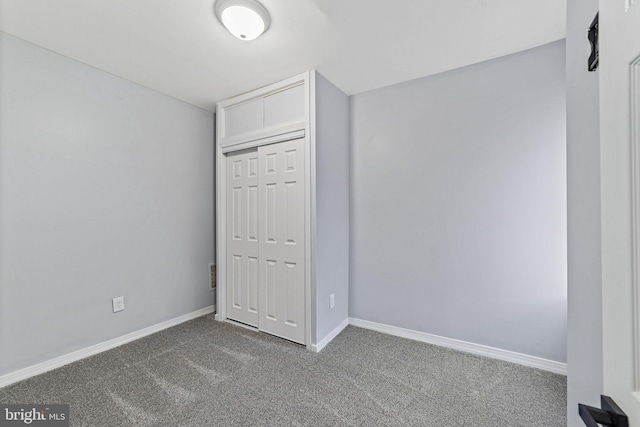 unfurnished bedroom with dark colored carpet, a closet, and baseboards
