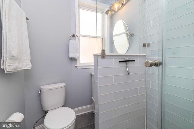 bathroom with a shower stall, toilet, and baseboards