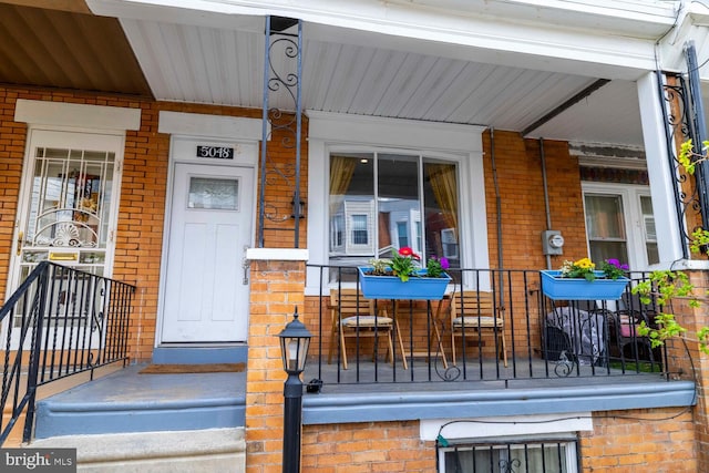 doorway to property with covered porch and brick siding