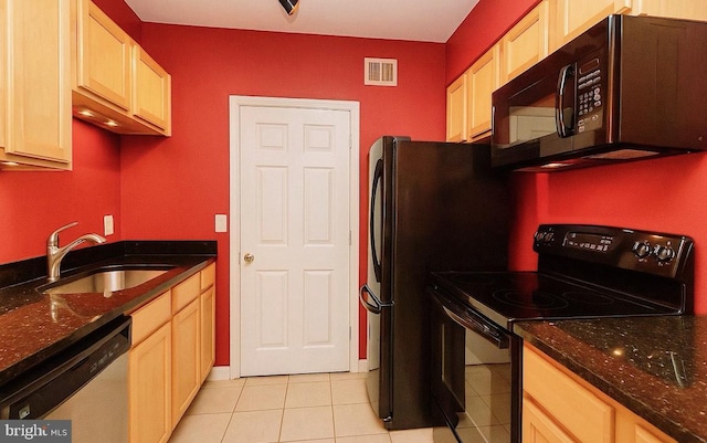 kitchen featuring a sink, dark stone countertops, light tile patterned floors, visible vents, and black appliances