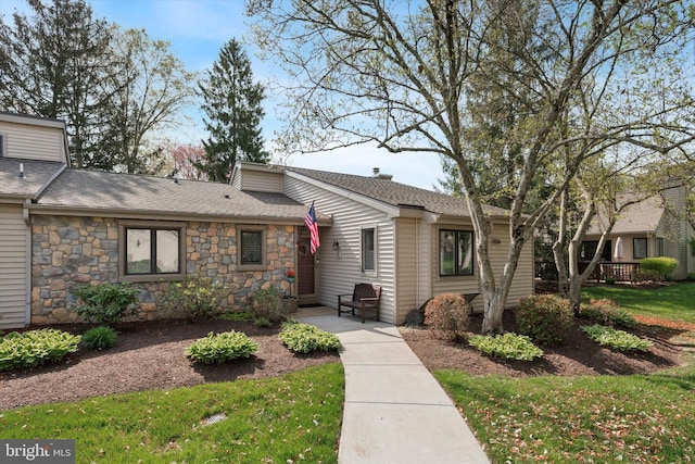view of front of property featuring roof with shingles, a front yard, and stone siding