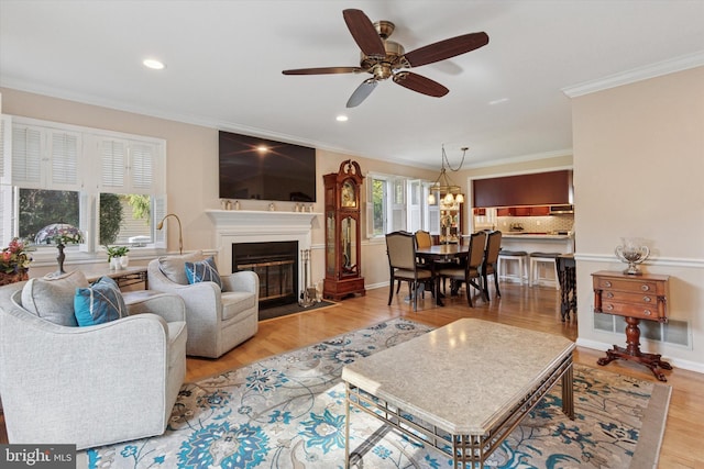 living room with recessed lighting, light wood-style floors, ceiling fan, a fireplace with flush hearth, and crown molding