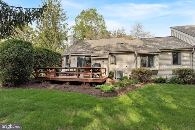 back of property with central air condition unit, a wooden deck, a chimney, a lawn, and roof with shingles