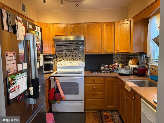 kitchen with tasteful backsplash, a sink, brown cabinetry, white appliances, and under cabinet range hood