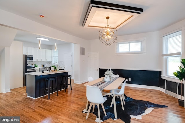 dining space featuring an inviting chandelier, a raised ceiling, light wood-style flooring, baseboards, and visible vents