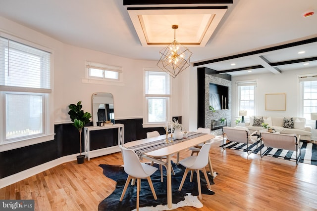 dining space with arched walkways, a fireplace, a raised ceiling, light wood finished floors, and a chandelier