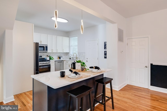 kitchen with pendant lighting, a breakfast bar, light wood-type flooring, white cabinetry, and appliances with stainless steel finishes