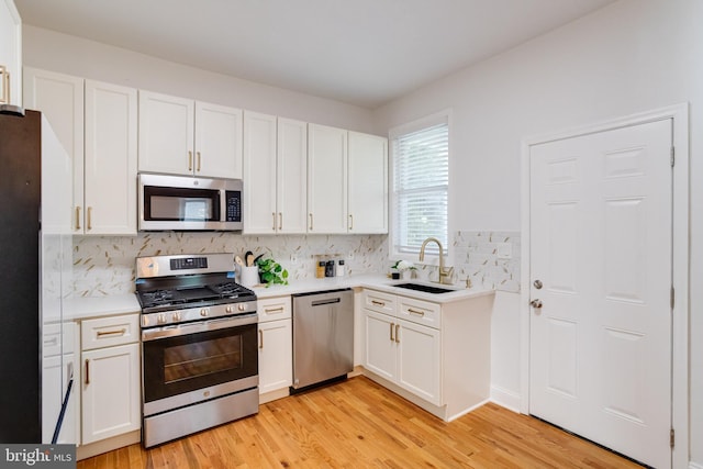 kitchen featuring stainless steel appliances, white cabinetry, a sink, and light wood-style flooring