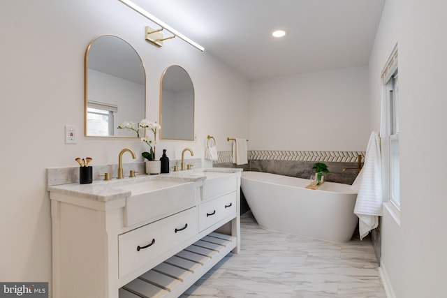 full bath with a sink, a freestanding bath, double vanity, and marble finish floor