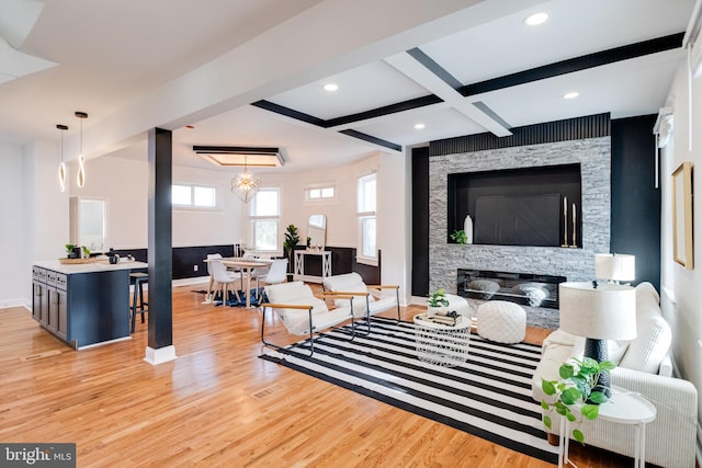 living area with beam ceiling, a stone fireplace, baseboards, coffered ceiling, and light wood finished floors