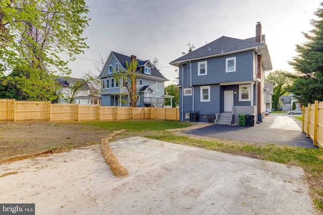 rear view of house with fence, a chimney, central AC unit, entry steps, and a residential view