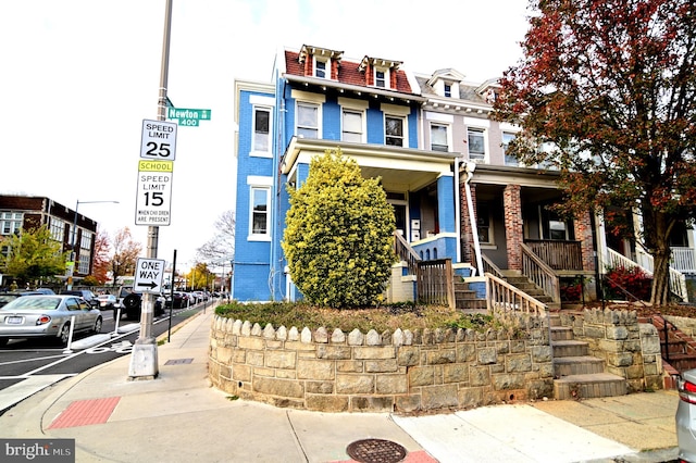 view of front of property with brick siding, a porch, stairs, and mansard roof