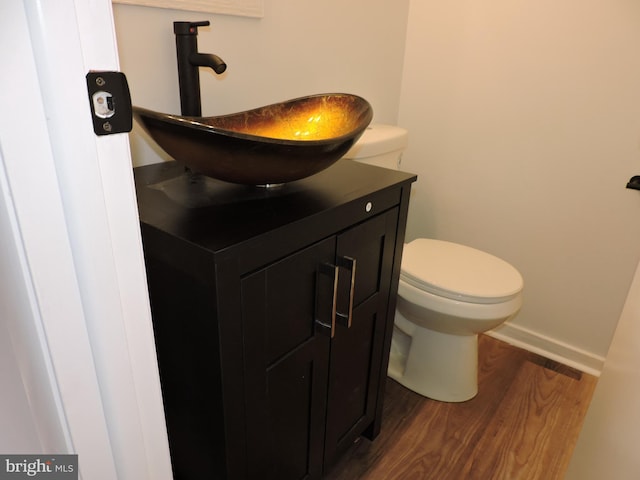 half bath with wood finished floors, vanity, toilet, and baseboards