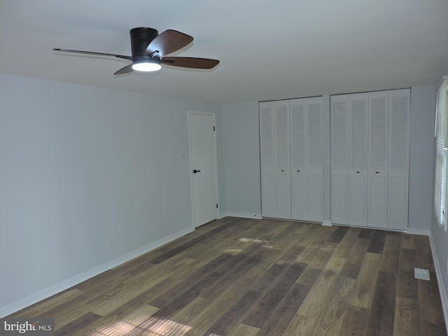 unfurnished bedroom with multiple closets, wood finished floors, baseboards, and a ceiling fan