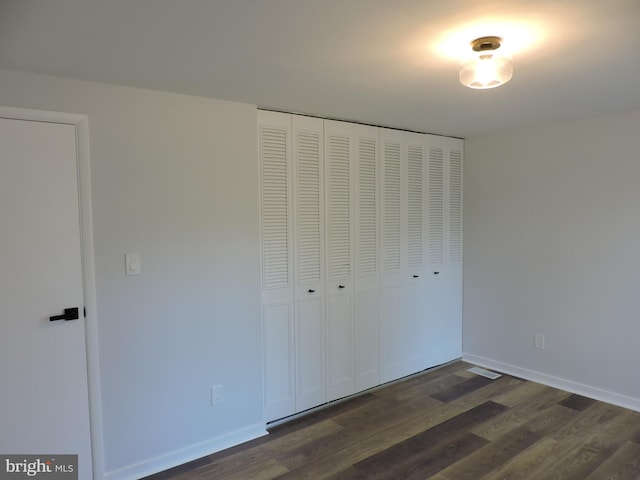 unfurnished bedroom featuring dark wood-type flooring, a closet, and baseboards