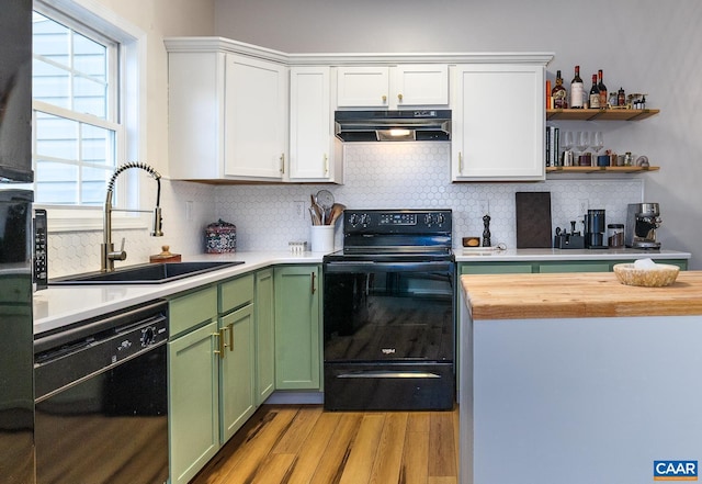 kitchen featuring a sink, black appliances, light wood-style floors, green cabinets, and under cabinet range hood