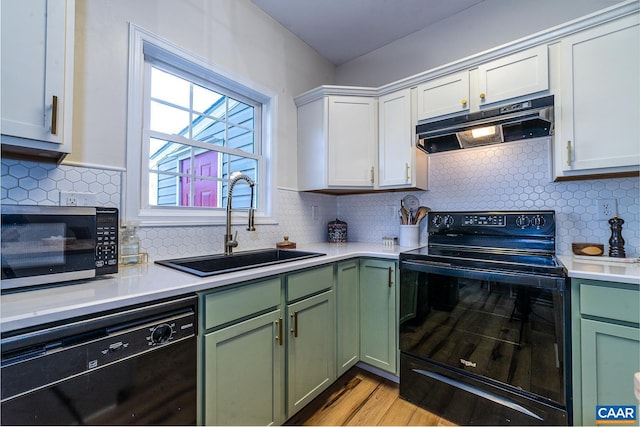 kitchen featuring a sink, green cabinets, light countertops, under cabinet range hood, and black appliances