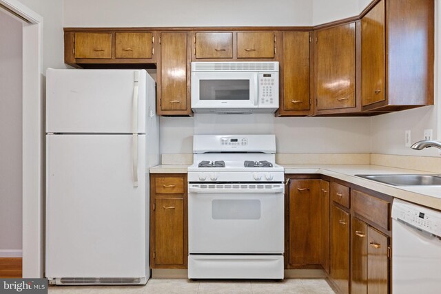 kitchen with white appliances, brown cabinetry, a sink, and light countertops