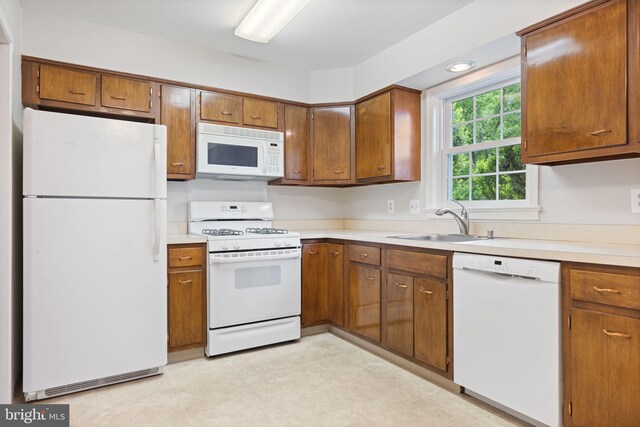 kitchen with a sink, white appliances, light countertops, brown cabinetry, and light floors