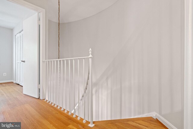 corridor with baseboards, an upstairs landing, and wood finished floors