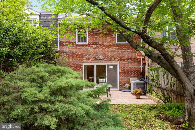 back of property featuring fence, cooling unit, mansard roof, brick siding, and a patio area