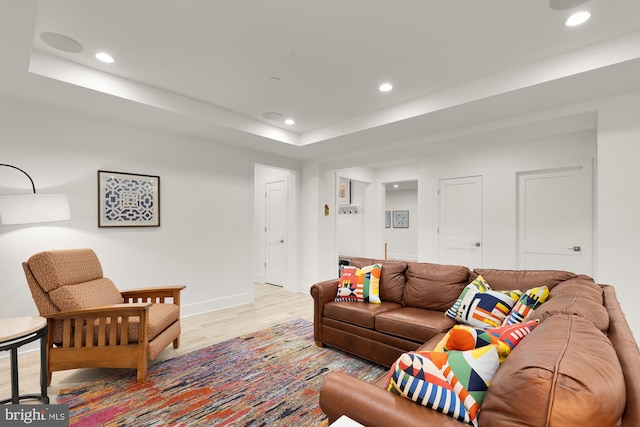 living room featuring recessed lighting, light wood finished floors, baseboards, and a tray ceiling