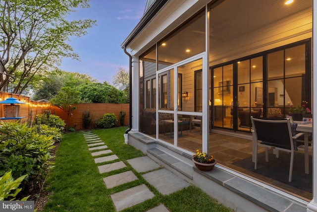 exterior space featuring fence, a sunroom, and a lawn